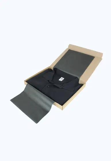 Open light brown corrugated mailer box with a neatly folded black polo shirt on dark tissue paper inside