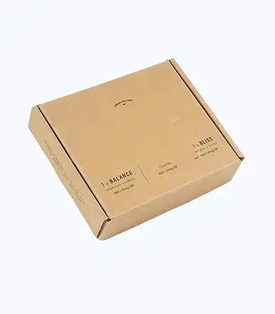Light brown corrugated cardboard shipping box with minimalist black text printing showing 'PREMIUM CBD', 'BALANCE', 'EVERYDAY FORMULA', 'BLISS', and 'STORAGE PODS' product details