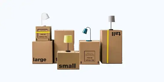 Arrangement of five brown cardboard moving boxes of varying sizes labeled 'large', 'small', and 'tall', with three modern table lamps with different colored shades placed on top